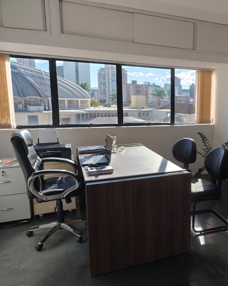 Mesa de madeira, cadeiras de atendimento e janela com vista para o Centro de Joinville na sala da Dra. Soeli Konell