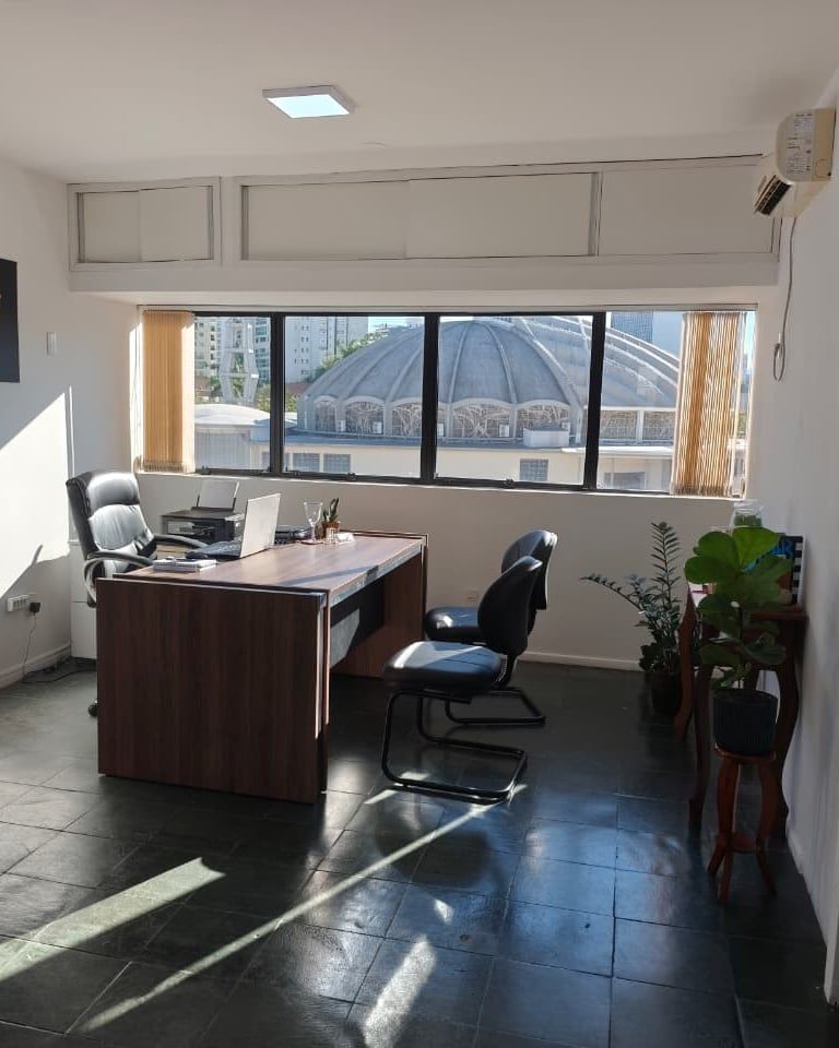 Mesa de madeira com notebook e cadeiras diante da janela na sala de atendimento do escritório em Joinville